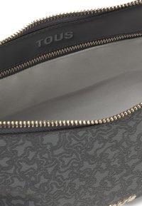 Borsa grigia con trama, chiusura a zip, hardware di colore oro e logo impresso. Interno con foderatura beige e design spazioso.
