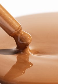 Bruine vloeistof met glanzende afwerking die uit een druppel stroomt. Gladde textuur, glanzend oppervlak en lichtreflectie creëren diepte.