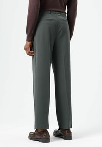 Donkergroene op maat gemaakte broek met een rechte pasvorm, voorzien van twee achterzakken en een gladde textuur, gecombineerd met bruine loafers.