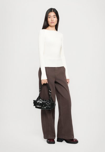 Ribbed white long-sleeve top, loose brown wide-leg trousers, and a small black bag with hardware details. Model stands in a neutral background.
