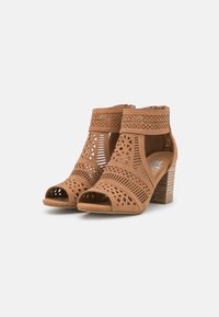 Sandalias de tacón marrones con diseños recortados, punta abierta y un upper texturizado y detallado. Tacón de bloque con un acabado natural parecido a la madera.