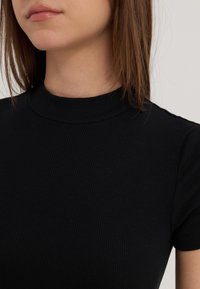 Schwarzes, geripptes Oberteil mit figurnaher Silhouette und hohem Kragen, das kurze Ärmel und einen glatten, strukturierten Stoff aufweist.