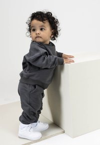 Grijze sweatshirt en broek gecombineerd met witte sneakers bij een kind. De outfit heeft een relaxte pasvorm en ribbelmanchetten; de overall textuur is glad.