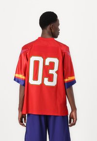 Red short-sleeve jersey made of synthetic fabric features large white number "03" on the back, with multicolored sleeve accents and a relaxed fit.