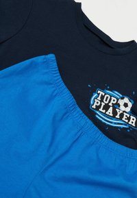Tričko s krátkým rukávem v námořnické modré barvě a jasně modré šortky. Obsahuje grafiku "TOP PLAYER" s fotbalovým míčem, elastický pas a měkký bavlněný materiál.