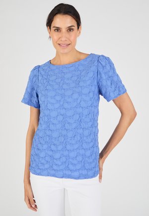 T-shirt bleu à texture avec des manches courtes, présentant un motif floral. Le tissu est léger, avec un col rond et une coupe décontractée.