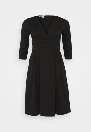 Robe noire en tissu lisse, avec un décolleté en V profond, des manches trois-quarts et une jupe plissée avec une fermeture éclair au dos.