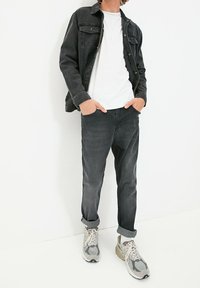 Giacca di denim nera sopra una maglietta bianca, abbinata a jeans scuri e sneakers grigie. Look casual con maniche arrotolate e dettagli nelle tasche.