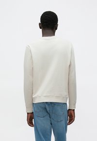 Ανοιχτό γκρι φούτερ από μαλακό ύφασμα, με στρογγυλή λαιμόκοψη και ριμπ μανσέτες. Φορεμένο με μπλε τζιν, που εμφανίζουν λεπτομέρειες πίσω τσέπης.