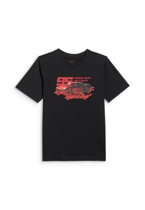 Chłopiec z krótkimi blond włosami, ubrany w czarny T-shirt z grafiką samochodu, czerwone spodnie dresowe, białe skarpety i czarno-białe trampki, stojący na białym tle.
