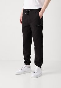 Zwarte joggingsbroek met een koord in de taille, cuffs bij de enkels en zijzakken. Heeft een geborduurd "Calvin Klein Jeans" logo in het wit.