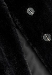 Tissu en fausse fourrure noire présentant une texture lisse, avec un gros plan d'un bouton transparent et d'une doublure sombre en dessous.