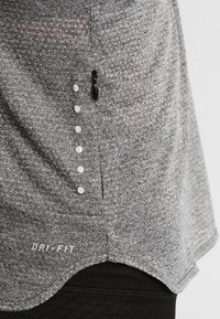 Grijze Dri-FIT shirt met een gestructureerd materiaal, een ronde zoom, een zijzak met rits en decoratieve witte geperste stippen langs de naad.