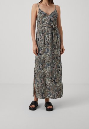 Kvinde iført en ærmeløs maxikjole med paisley-mønster, sidelommer og sorte slip-on sandaler mod en ensfarvet baggrund.