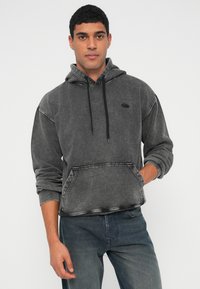 Γκρι βαμβακερό φούτερ με κουκούλα, τσέπη καγκουρό, ρυθμιζόμενο κορδόνι στην κουκούλα και ραφές σε αντίθετο χρώμα. Το μοντέλο το φοράει με σκούρα τζιν.