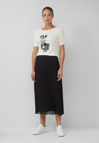 Top bianco a maniche corte con stampa zebrina nera e dorata, abbinato a una gonna midi plissettata nera e scarpe da ginnastica bianche. Design semplice e moderno.