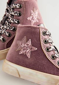 Rosa sammetshögskor med glittrande stjärnapplikationer, mönstrade snören och gummisula. Anmärkningsvärd textur och färgdetalj.