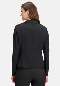 Schwarze taillierte Blazerjacke mit strukturiertem Design, langen Ärmeln und einem einzigen Knopfverschluss an der Vorderseite, ausgestattet mit glattem Stoff und subtilen Nähten.