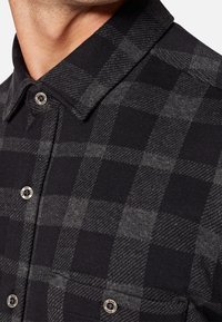 Zwart en grijs geruit overhemd met een gestructureerde kraag, metallic knopen en een zachte, textuurstof. Duidelijke ruitpatroon details.