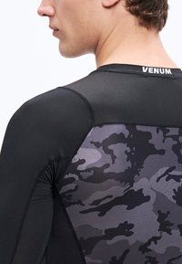 Czarny sportowy T-shirt o dopasowanym kroju, wykonany z teksturowanej tkaniny, z tyłem w kamuflażowym wzorze w odcieniach szarości. Logo "VENUM" na kołnierzu.