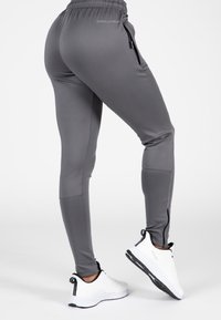 Grijze sportleggingen met een strakke pasvorm, ritszakken en een hoge tailleband, gecombineerd met witte schoenen met zwarte accenten.