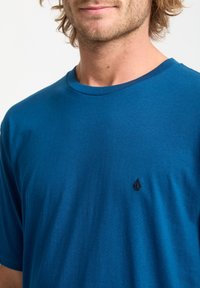 Blaues Baumwoll-T-Shirt mit kurzen Ärmeln und Rundhalsausschnitt. Mit einem kleinen schwarzen Logo auf der Brust. Weicher Stoff, lässige Passform.