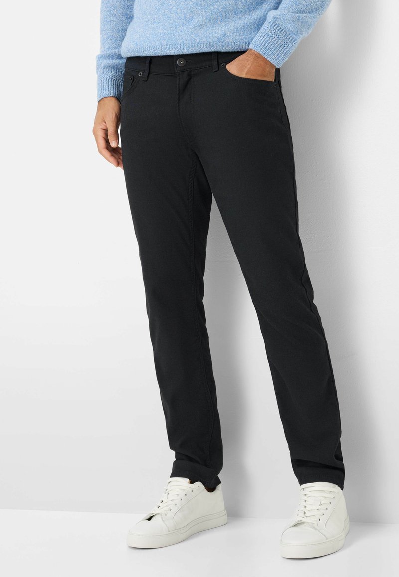 Zwarte stoffen broek met een slim fit, voorzien van een knoopsluiting, zijzakken en gecombineerd met witte sneakers. Boven een gebreide trui met een textuur.