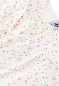Weißes Baumwollkleidungsstück mit bunten Polka-Dots in Rot, Pink, Gelb und Blau. Verfügt über einen Knopfverschluss und Raffung.