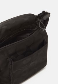 Black nylon shoulder bag with a subtle floral pattern, featuring a zippered main compartment and an exterior pocket for organization.
