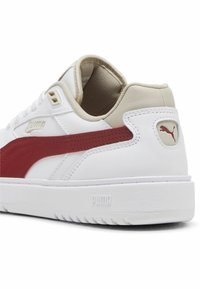 Baskets en cuir blanc avec une bande en suédine rouge, des accents beige et une semelle en caoutchouc texturé. Comprend un détail de logo au niveau du talon et sur le côté.