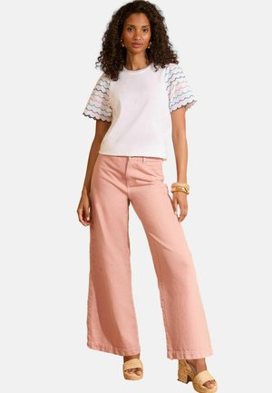 Top bianco con maniche a scallop colorate, abbinato a pantaloni rosa a gamba larga e sandali con zeppa color marrone chiaro. Tessuto morbido e vestibilità rilassata.
