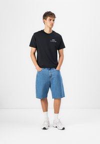 Black cotton t-shirt with "new balance" logo, paired with blue denim shorts and white sneakers. Simple, casual design; relaxed fit.
