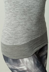 Top de tirantes ajustado en gris con un acabado texturizado, que presenta un dobladillo acanalado, combinado con leggings estampados en colores oscuros y tonos de gris.