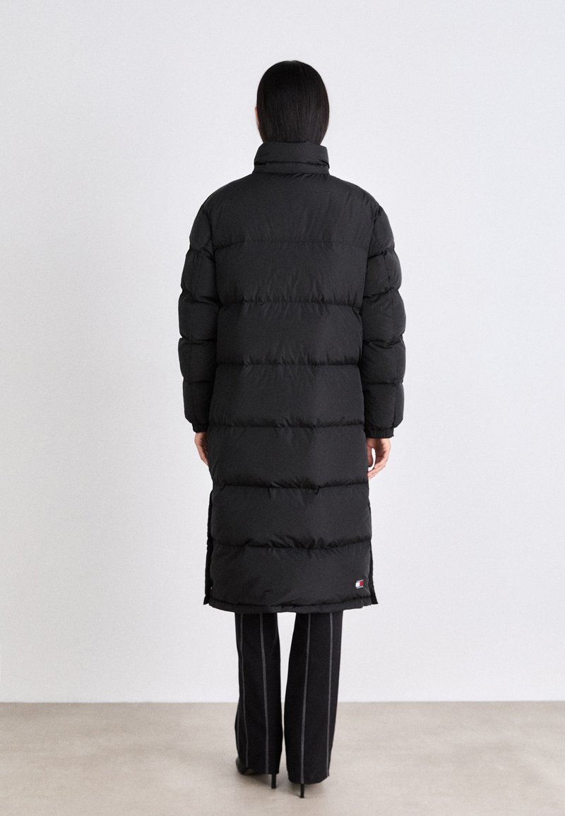 Schwarze Daunenjacke mit horizontaler Steppung, hohem Kragen und seitlichen Schlitzen. Das Material wirkt glatt und isoliert für Wärme.