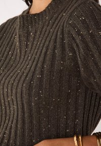 Pull marron foncé côtelé avec des paillettes métalliques. Caractérisé par une encolure ronde et un tissu texturé avec des lignes en relief. Comprend des accents de ferrures métalliques.