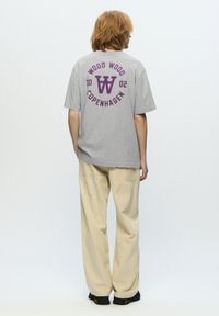 Grå bomulds t-shirt med et rundt lilla grafisk design, der har "WOOD WOOD," "COPENHAGEN," og "2002" på ryggen. Løs pasform.