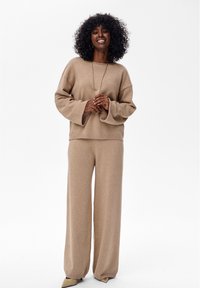 Beige gebreide trui met brede mouwen, gecombineerd met bijpassende losvallende broek met subtiele glans, ontspannen silhouet en geribbelde manchetten.