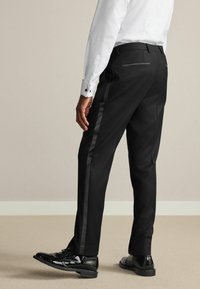 Black dress pants with a straight cut, featuring a glossy black side stripe and two rear pockets, paired with polished black shoes.