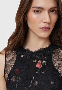 Black lace dress featuring floral embroidery, intricate lace neckline, and sheer lace accents on shoulders for added texture and detail.