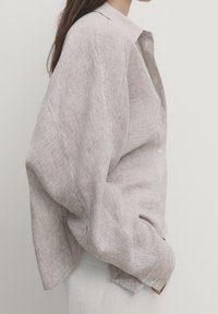 Randig långärmad skjorta i ljusbrun och kräm. Har en klassisk krage, lös passform och textil med synlig sömnad.