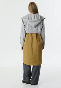 Grauer, verkürzter Kapuzenpullover, kombiniert mit einem senfgelben, langen Rock. Das Outfit hat einen Kordelzugbund und eine lässige Passform.