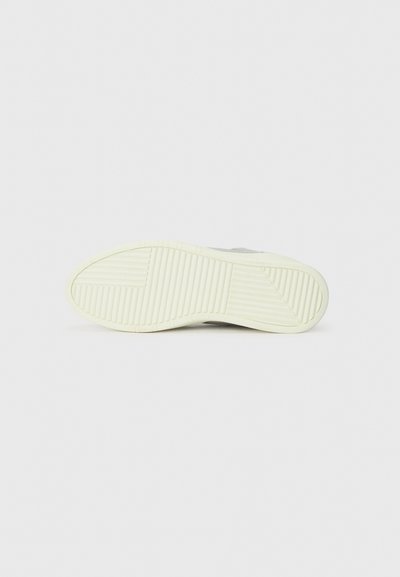 White sneaker sole with vertical and horizontal grooves, featuring a light cream-colored accent. Textured for traction and durability.