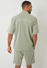 Chemise à manches courtes en tissu éponge vert clair avec col, associée à un short assorti. Texture lisse et coupe décontractée, adaptée à une tenue décontractée.