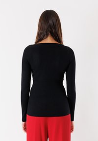 Maglietta nera a maniche lunghe con una silhouette aderente, caratterizzata da un collo a barchetta e un design senza cuciture, abbinata a pantaloni rossi.