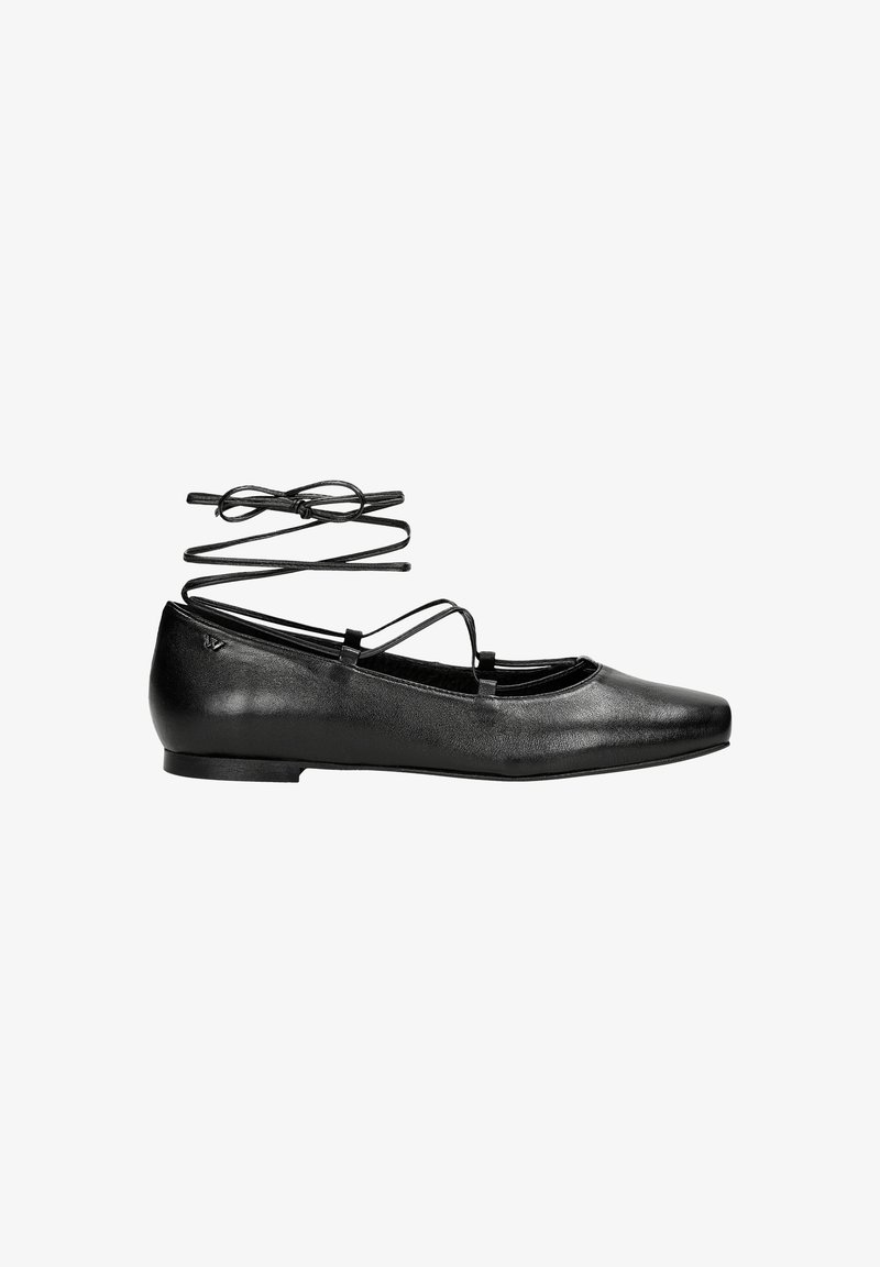 Ballerine en cuir noir avec bout pointu et fines lanières enroulées autour de la cheville et nouées en un noeud, vue de côté sur fond blanc.