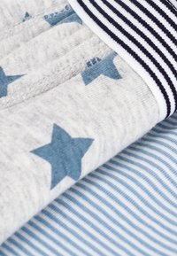 Tissu en coton avec une base gris clair ornée d'étoiles bleues et d'une ceinture rayée bleu marine. Texture douce et finition lisse dans l'ensemble.