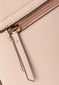 Beige Kunstledertasche mit einem goldenen Reißverschluss und braunen Akzenten, ausgestattet mit einem strukturierten Reißverschluss-Organizer und kontrastierenden Nähdetails.