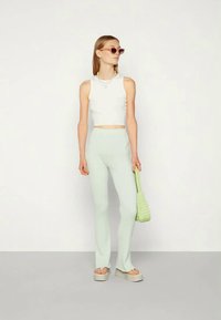 Top cropped branco, calças flared caneladas verde claro, sandálias de plataforma e uma pequena bolsa de palha. As acessórios incluem óculos de sol e brincos.