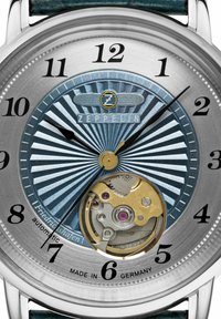 Round metallic watch with a blue radial patterned dial, black numerals, gold accents, and a visible automatic movement at the bottom.