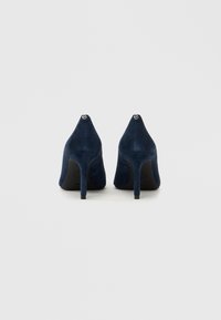 Temno modre semiš pete z ostro konico in vitkim peto, z majhnim logotipom na zadnji strani. Gladek tekstura.